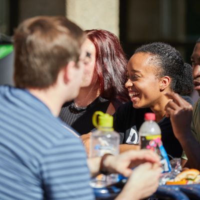 Students sat at a table chatting on lakeside terrace on a sunny day